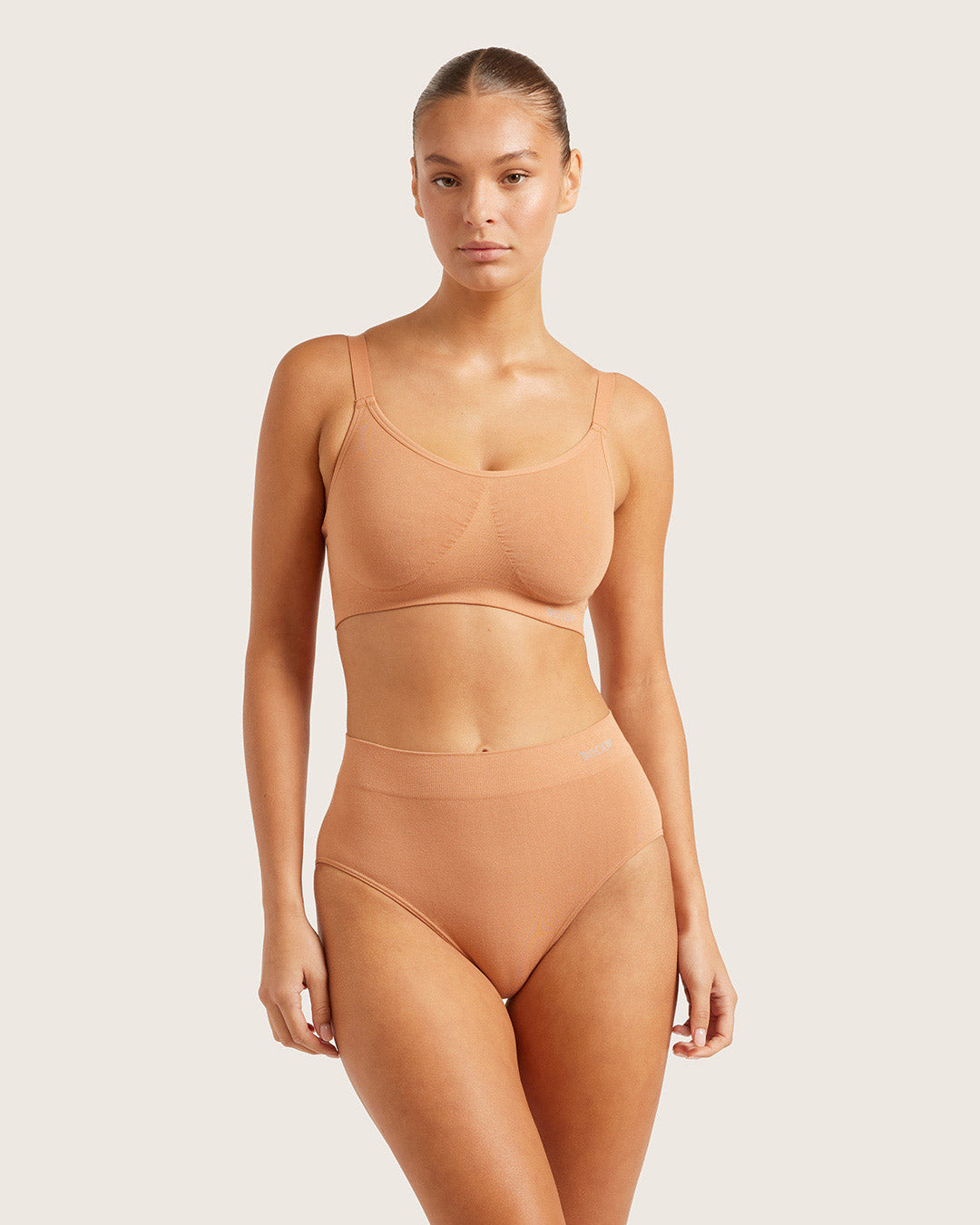 Woman wearing a beige underwear set against a plain background
