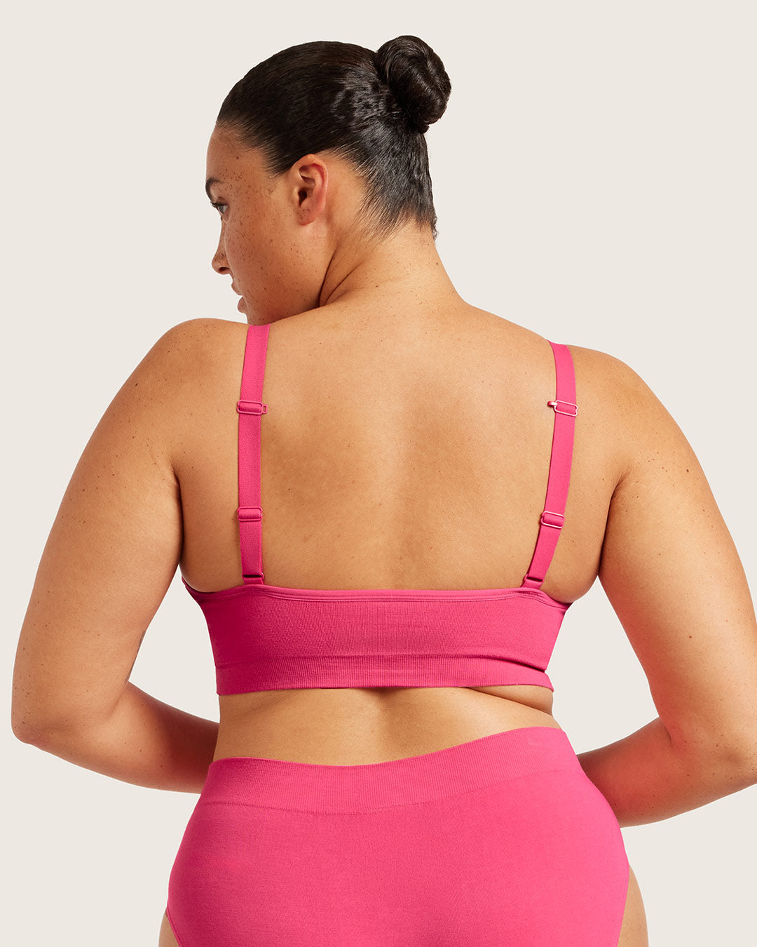 Person wearing pink bra and pink underwear on beige background