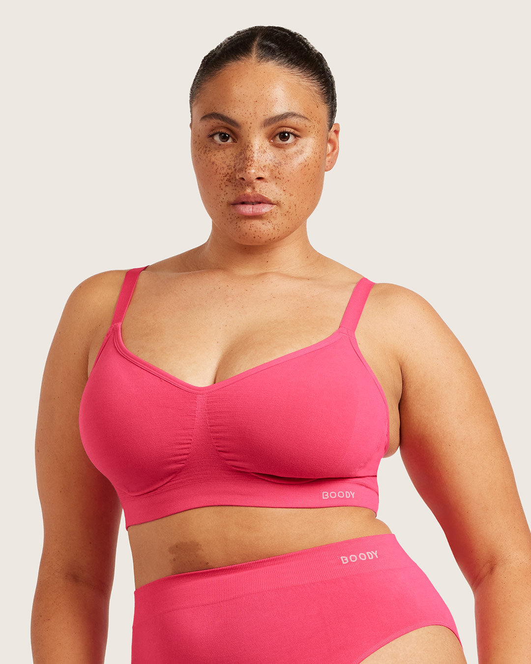 Woman wearing a pink bra and panty set on a light background