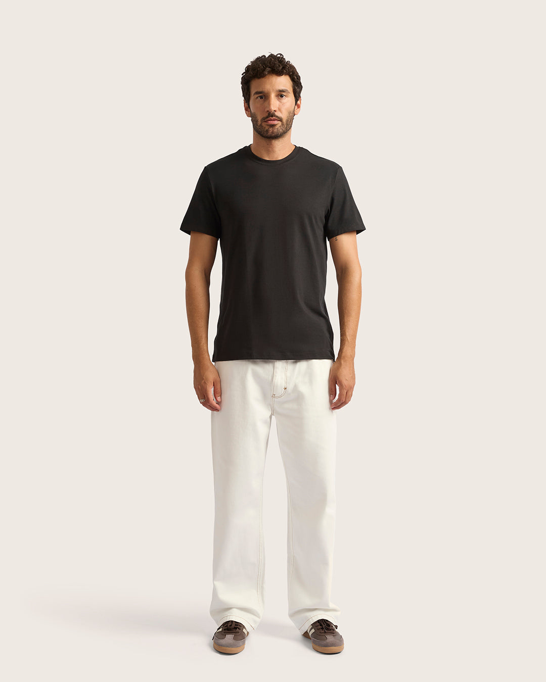 Man wearing a black t-shirt and white pants on a plain background