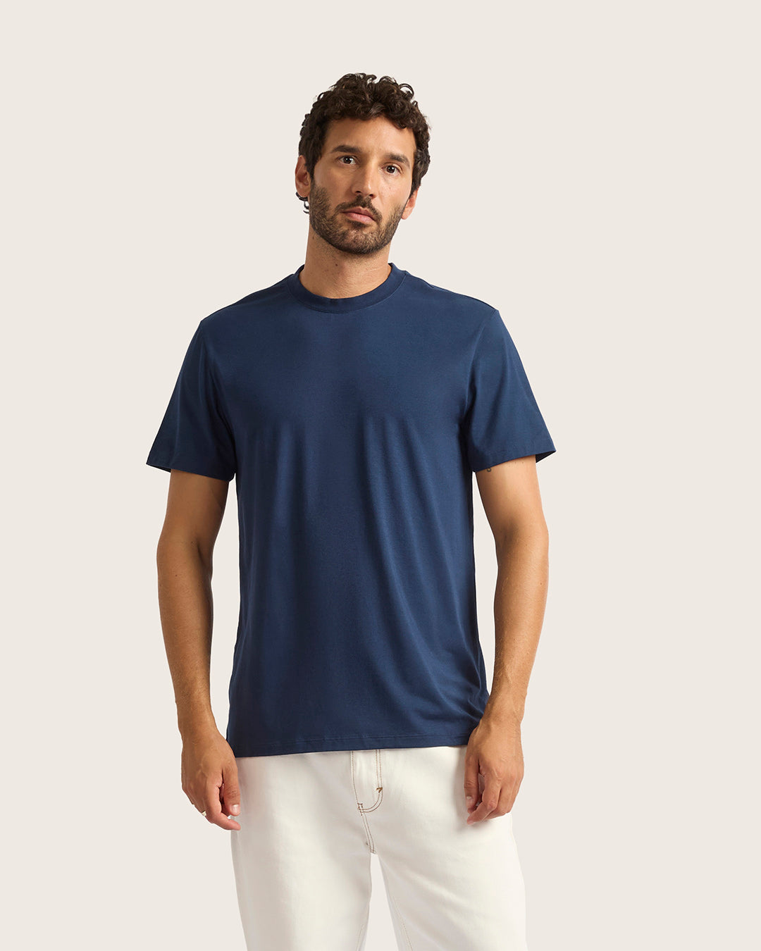 Man wearing a navy blue t-shirt and white pants on a light background