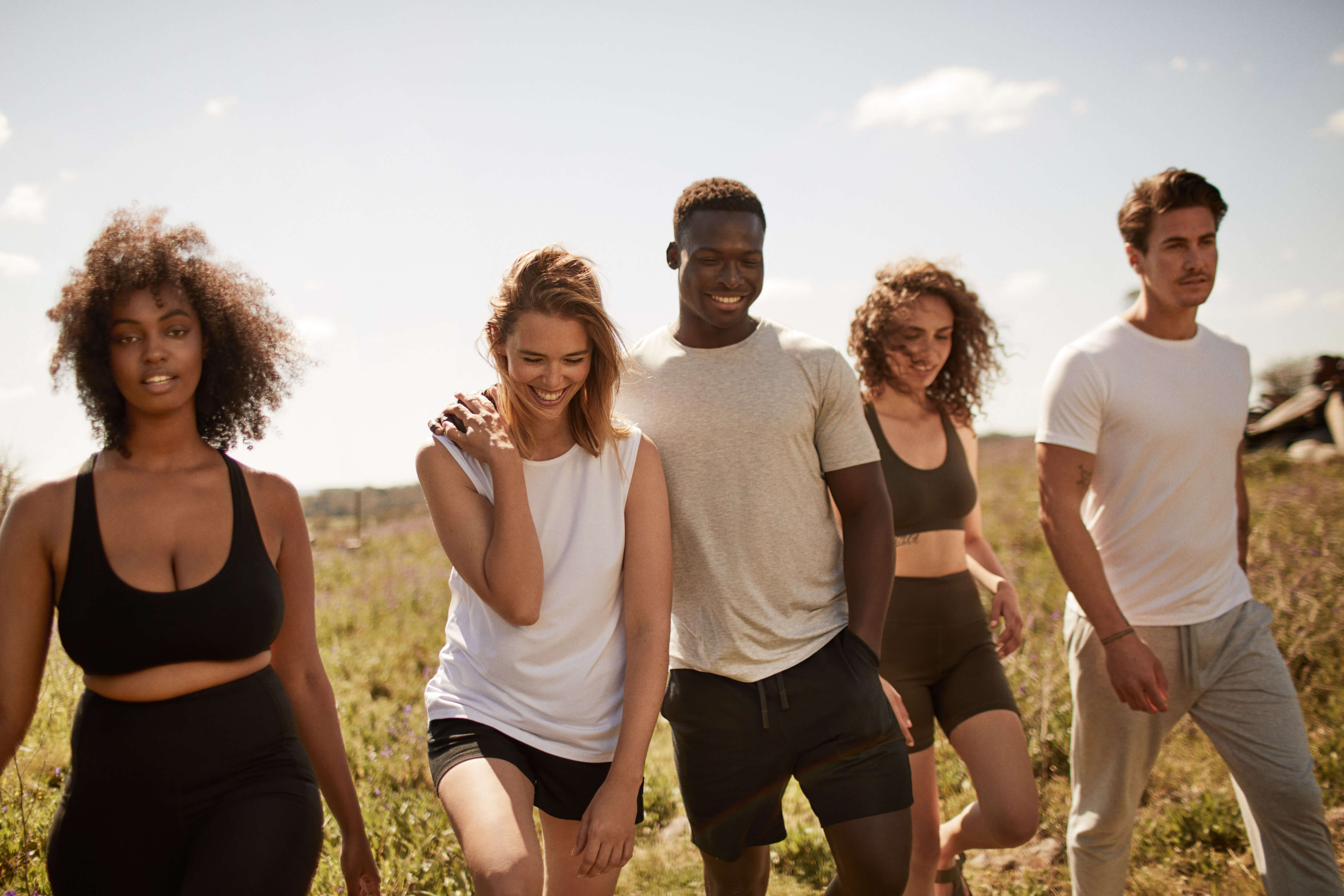 Group of five people walking together in a field on a sunny day