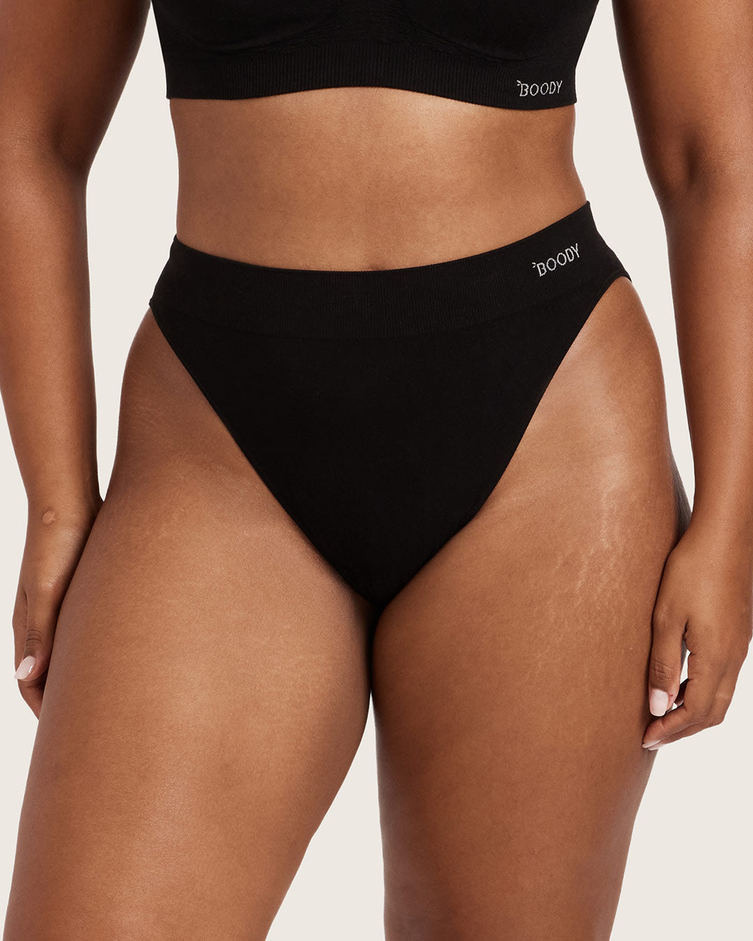 Person wearing black high-waisted bikini bottoms with 'Boody' branding on a neutral background