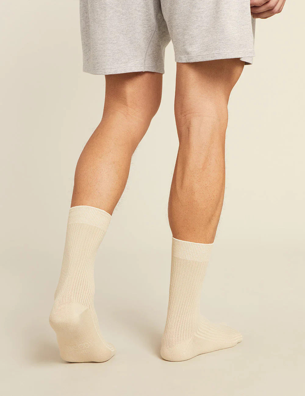 Person wearing beige socks and gray shorts on a plain background
