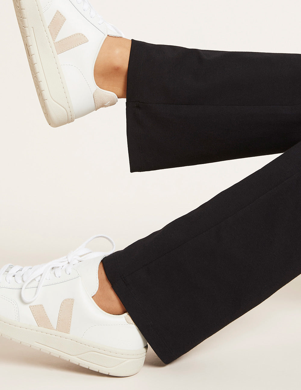 Person wearing black pants and white sneakers with a brand logo on a light background