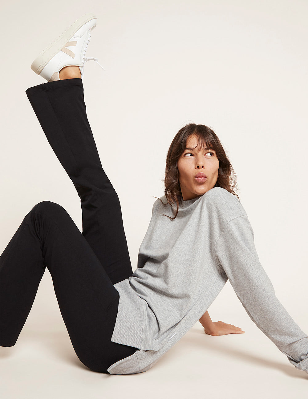 Person wearing black leggings and gray sweater on a white background