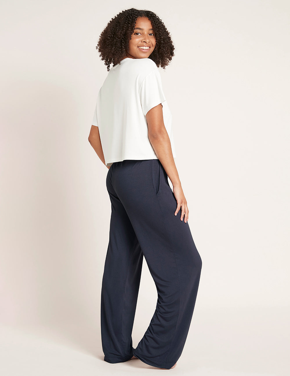 Woman wearing a white top and navy wide-leg pants on a plain background