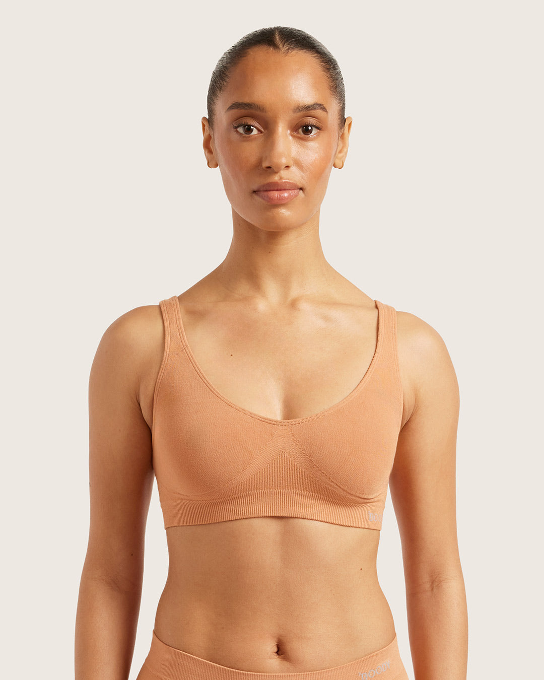Woman wearing a beige crop bra on a light pink background