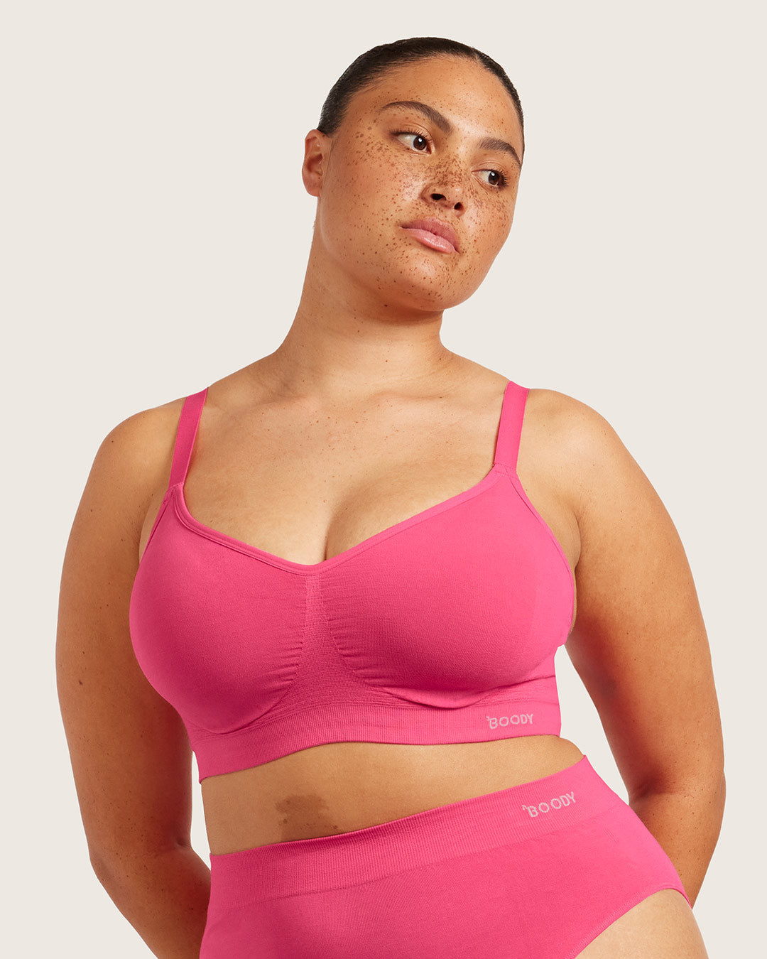 Woman wearing a pink bra on plain background.