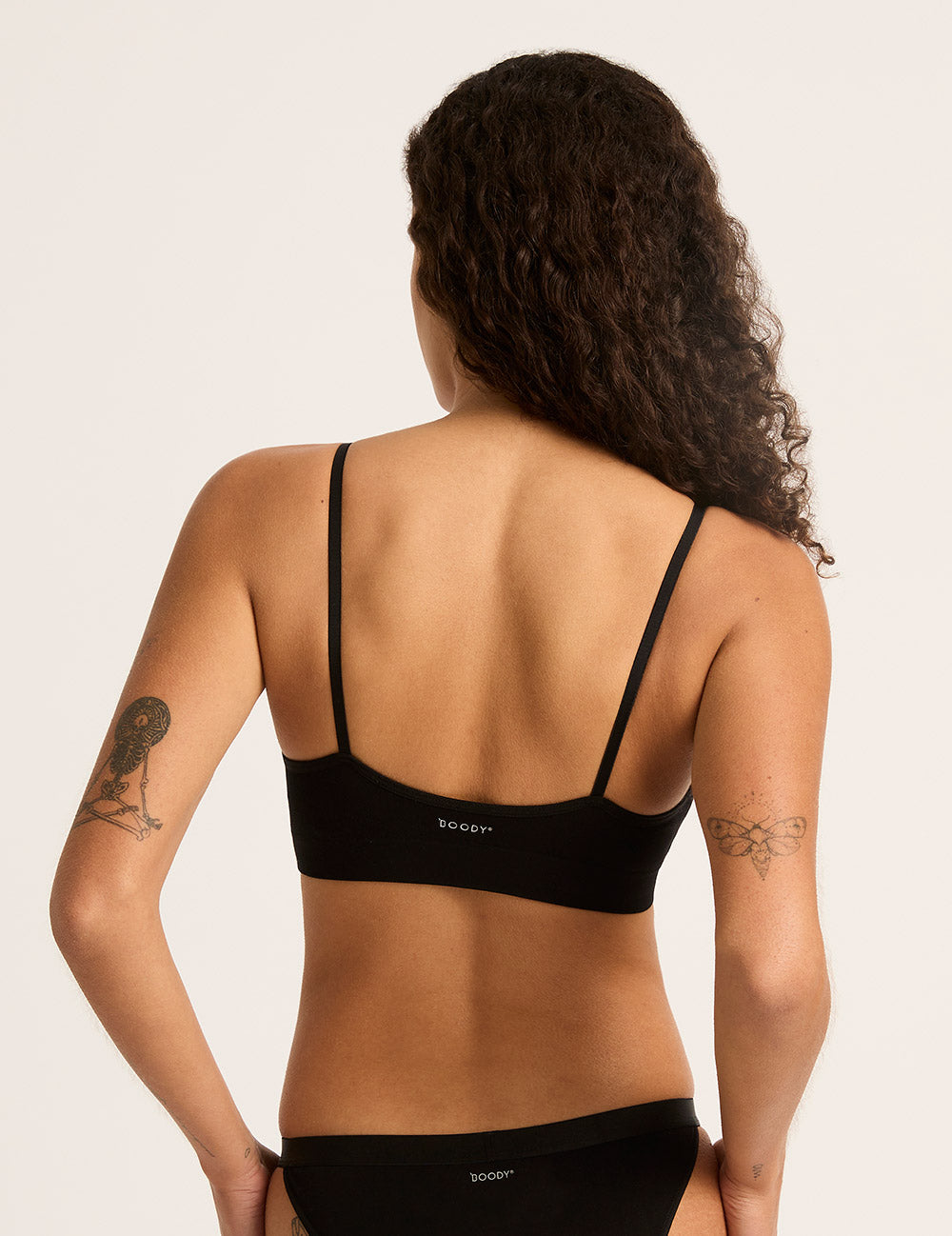 Woman wearing a black bralette with visible brand logo on a beige background