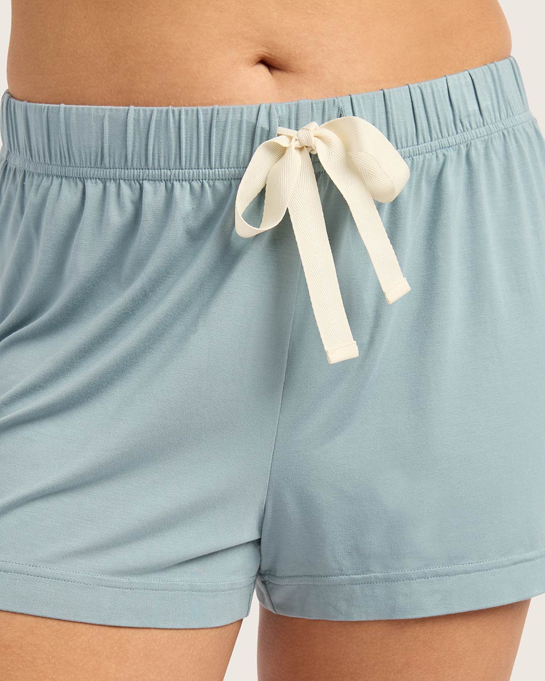 Light blue shorts with a cream ribbon tie on a neutral background