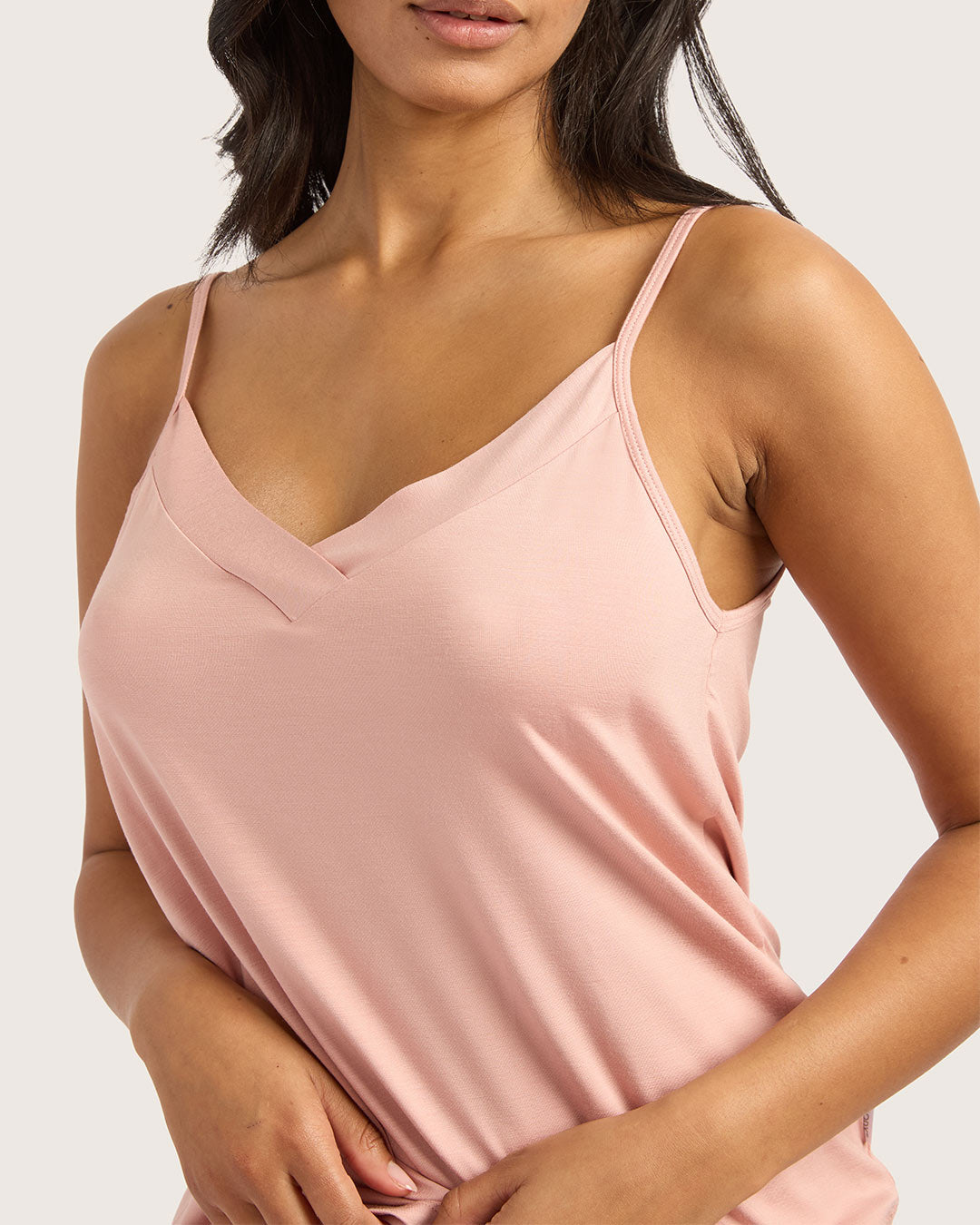 Woman wearing a pink spaghetti strap top against a neutral background