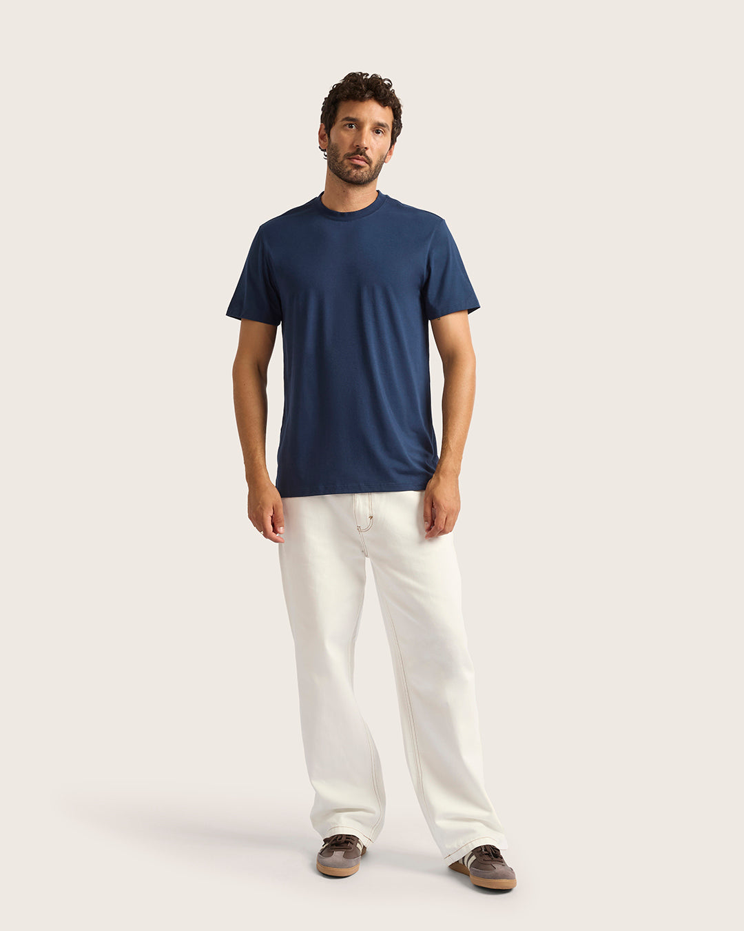 Man wearing a navy t-shirt and white pants on a light gray background