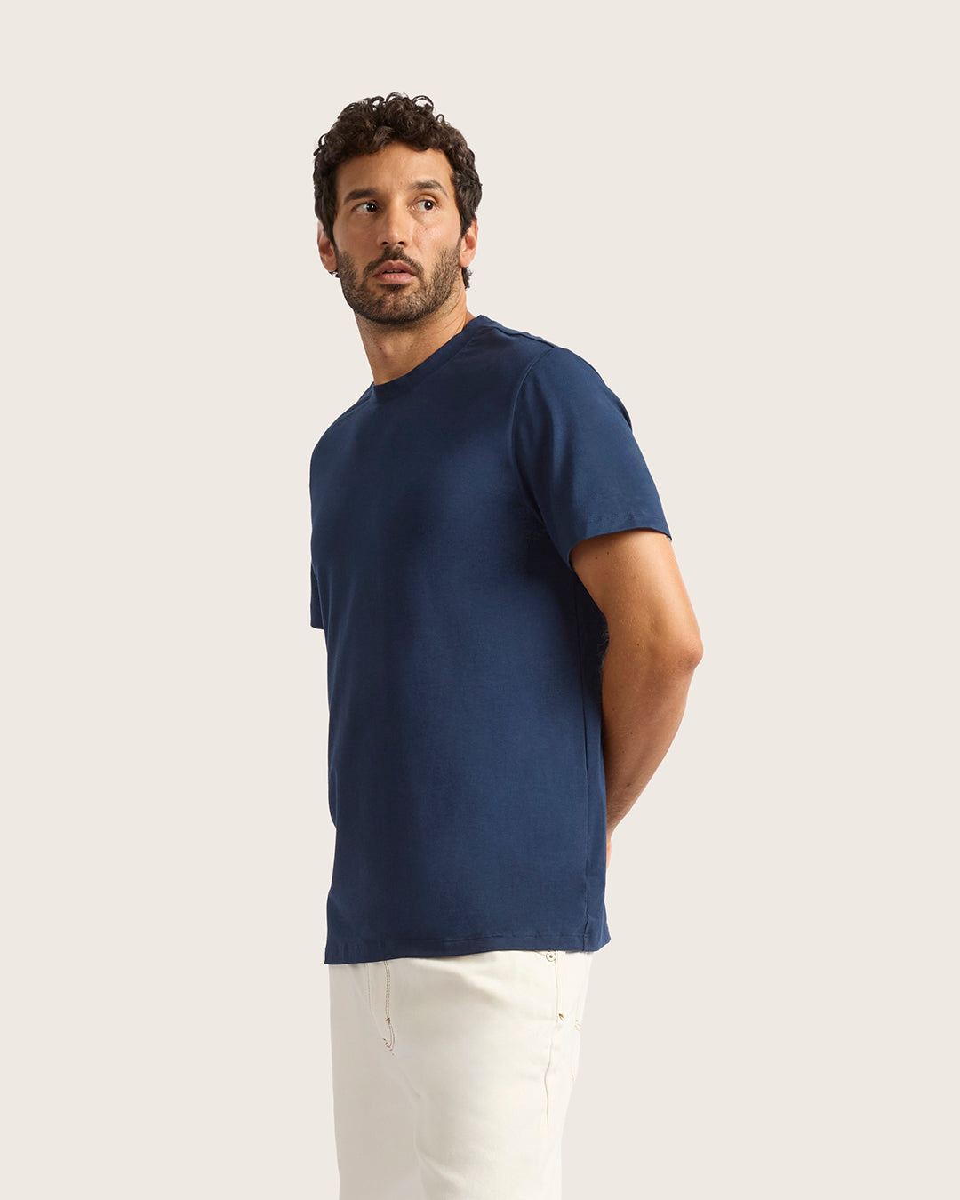 Man wearing a navy blue t-shirt and white pants on a light beige background