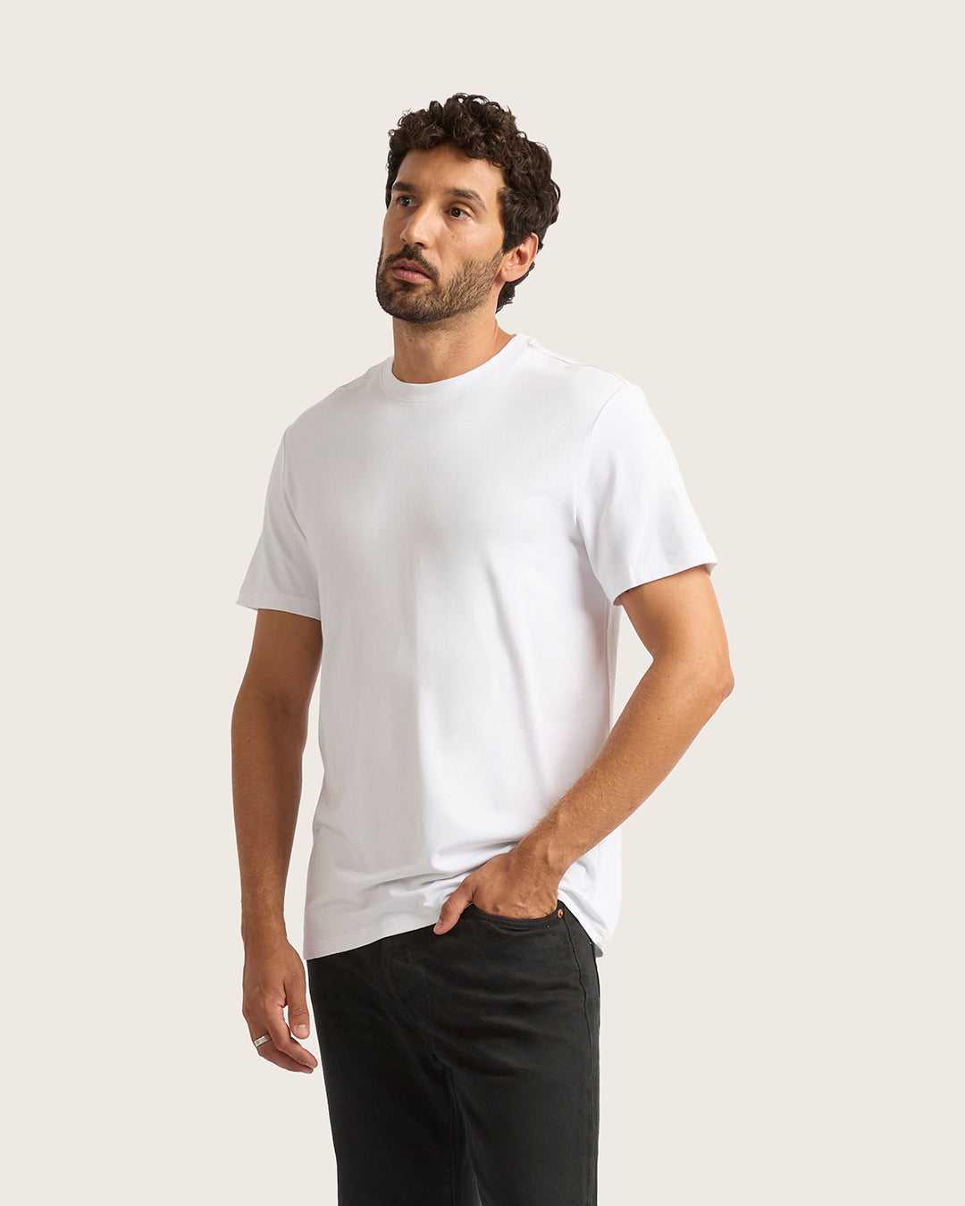 Man wearing a plain white t-shirt and black pants on a light background