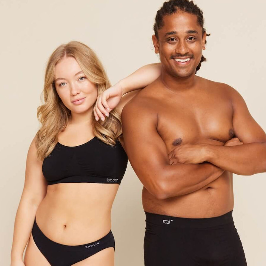 Man and woman wearing black swimwear standing against a beige background