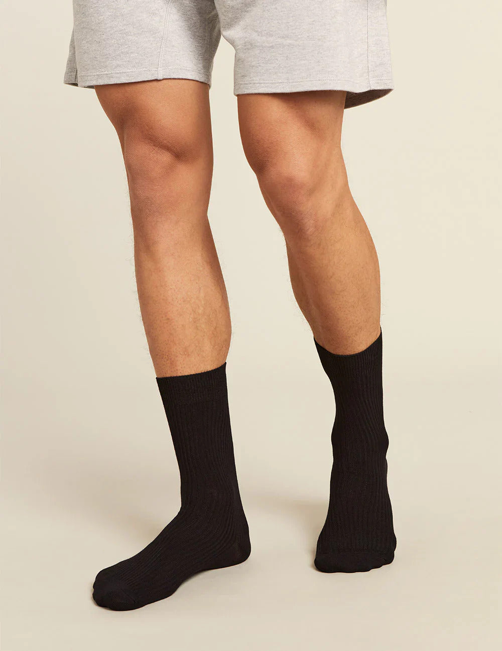 Person wearing black socks and gray shorts on a beige background