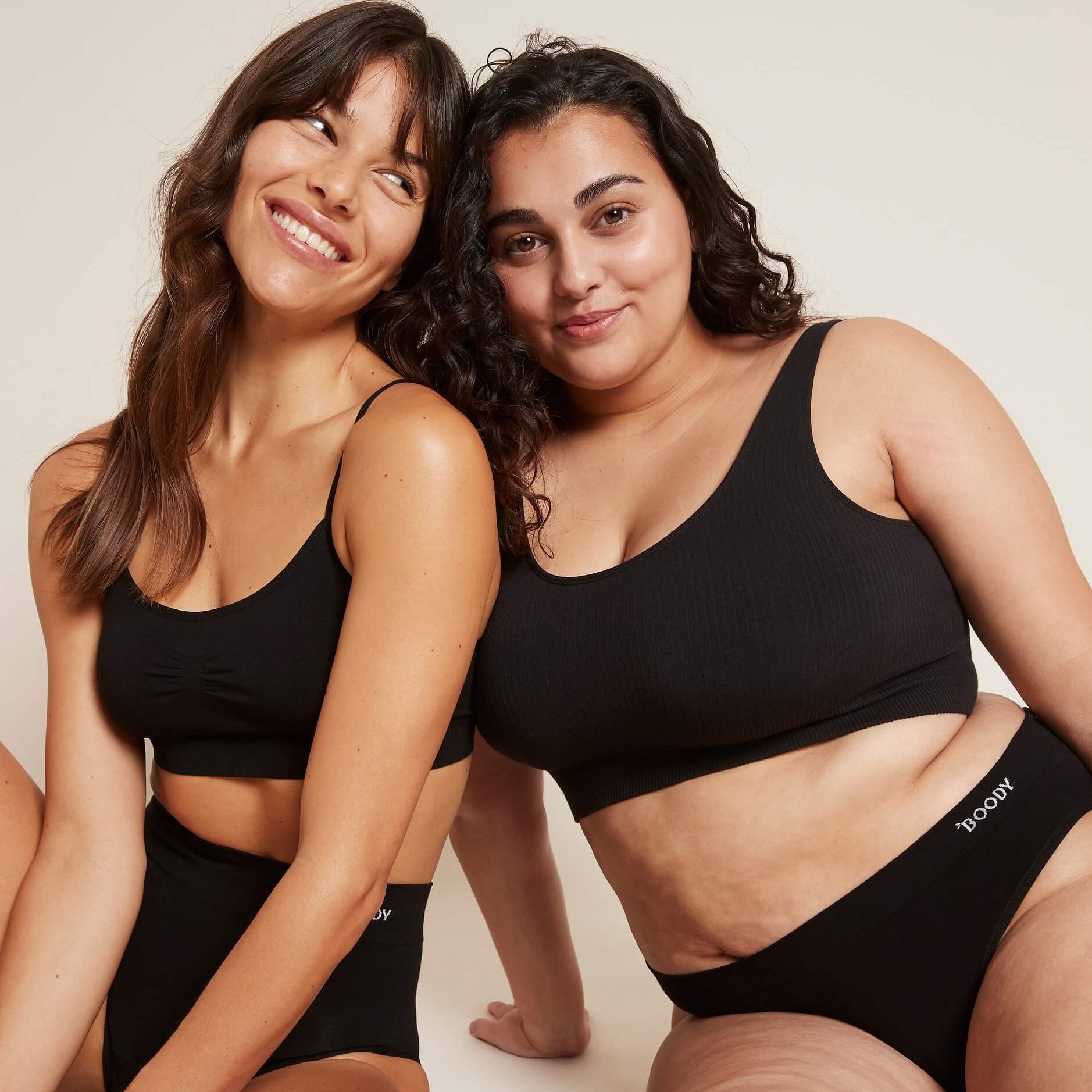 Two women wearing black athletic wear sitting on a light background