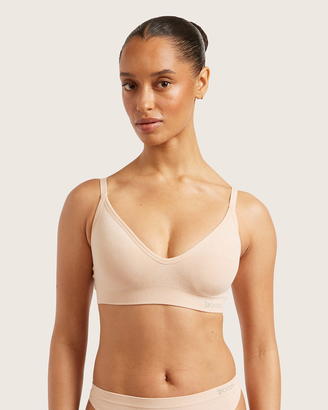 Woman wearing a beige bra and underwear set against a plain background